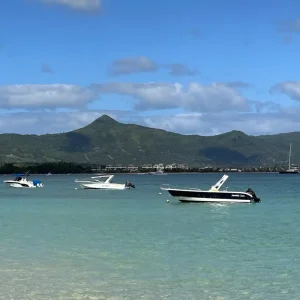 Speedboats anchored in turquoise lagoon with mountains from La Preneuse Beach, Mauritius