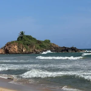 Waves crashing around rocky island with lush vegetation at Mirissa Beach, Sri Lanka