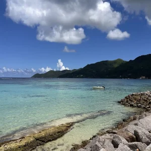 White boat anchored in turquoise lagoon with mountainous coastline in Seychelles