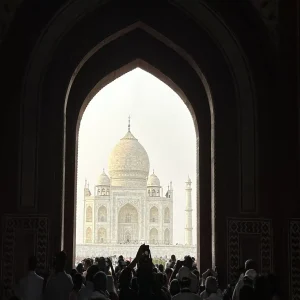 Taj Mahal viewed through Mughal archway with tourist crowds in Agra, India