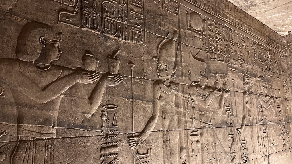 Detailed stone reliefs of ancient Egyptian figures and hieroglyphs on an interior wall at Philae Temple in Aswan, visited on Day 4 of a 10-Day Egypt Itinerary.